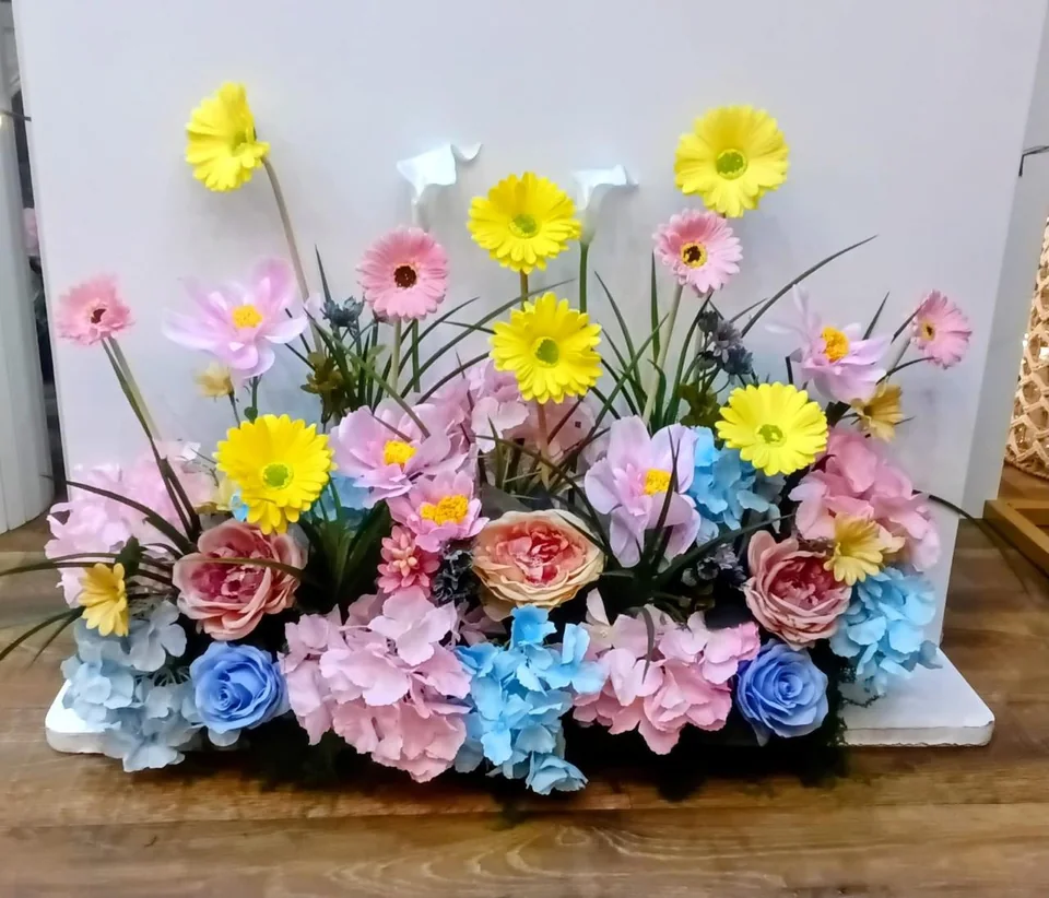 Colorful artificial flower arrangement with pink, yellow, blue and white blooms in a low rectangular base