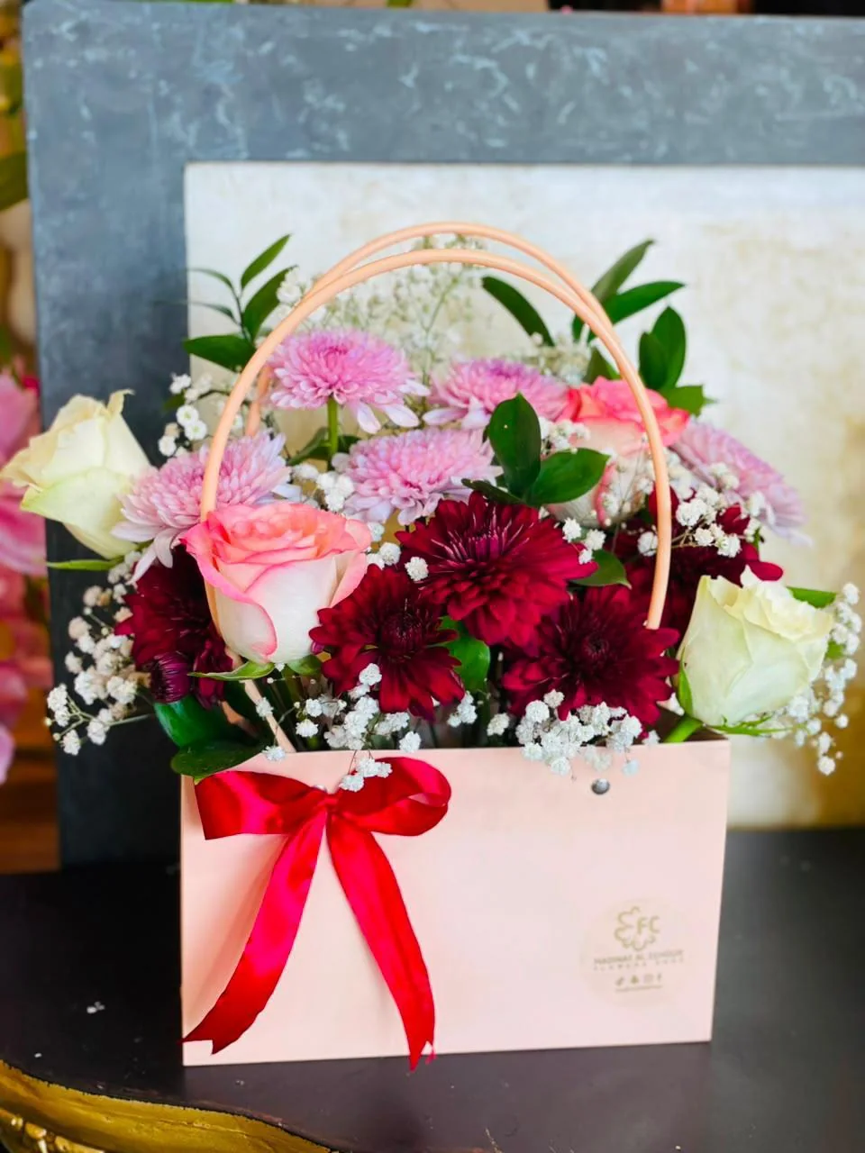 Baby-pink handled flower bag filled with red, pink and white blooms