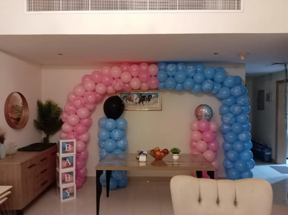 Pink and blue gender-reveal balloon arch with BABY blocks
