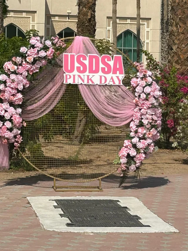 Outdoor celebration arch with pink flowers, draped fabric and a custom sign