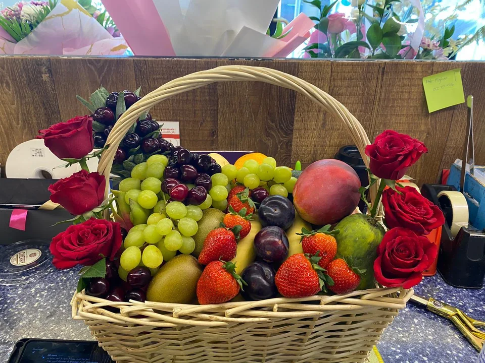 Wicker gift basket filled with assorted fruit and red roses