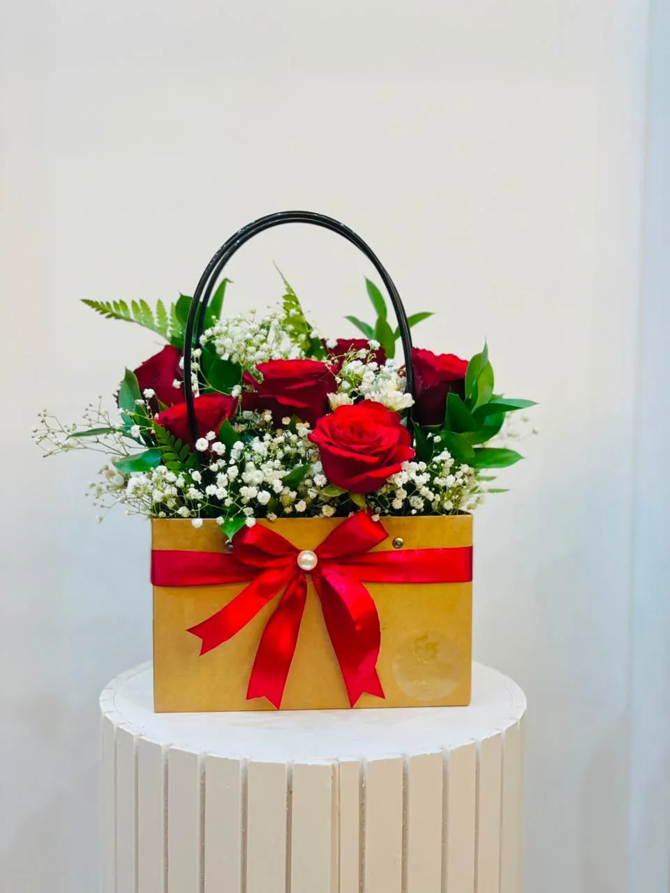 Golden handled flower bag with red roses, white filler flowers and a red bow