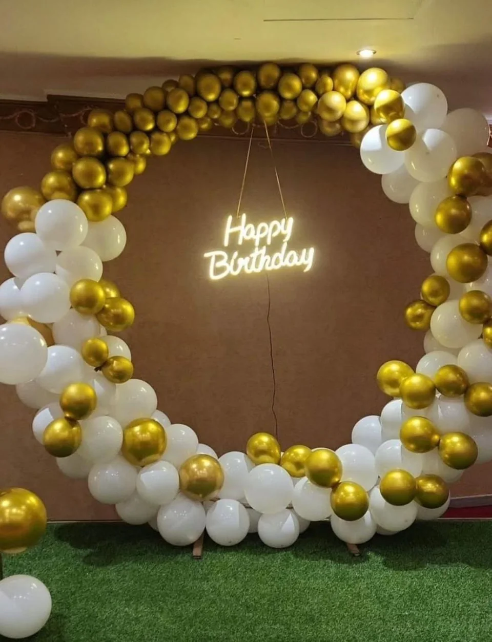 Circular gold and white balloon birthday arch with an illuminated Happy Birthday sign