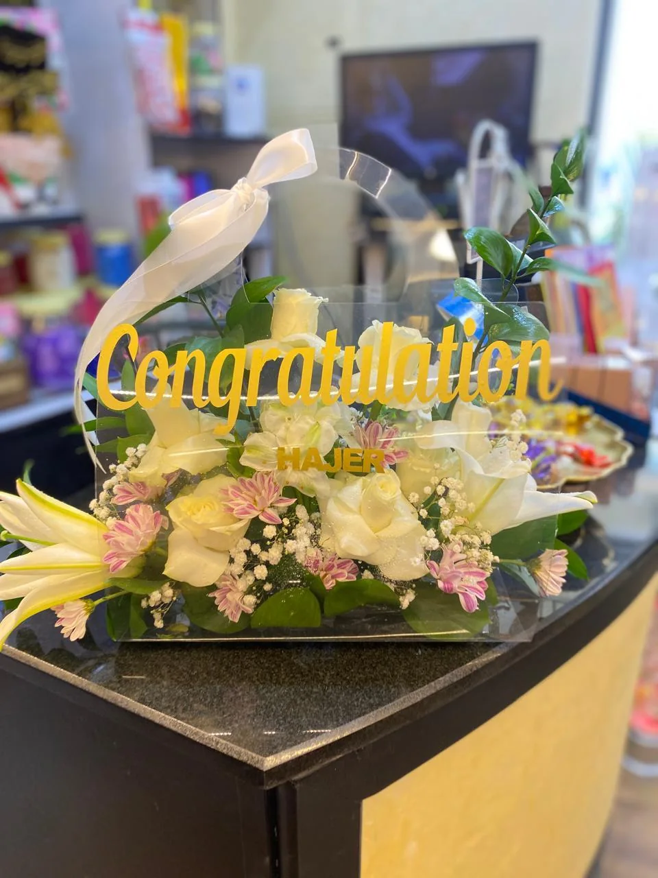Transparent congratulatory flower bag with white blooms, a name and a Congratulations topper