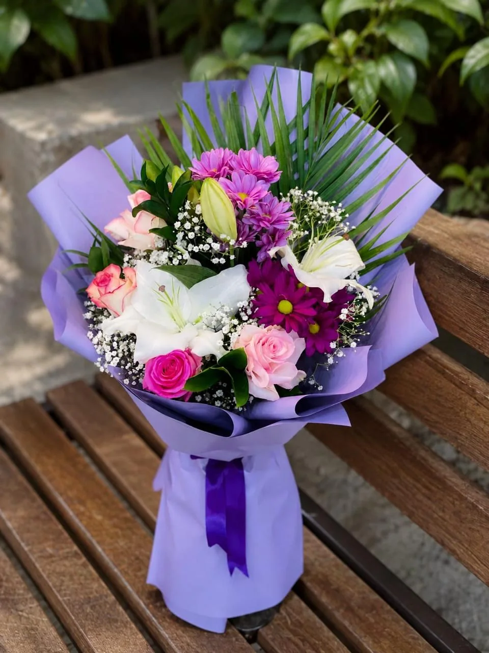 Purple-wrapped island lily bouquet with white lilies, pink blooms and palm leaves
