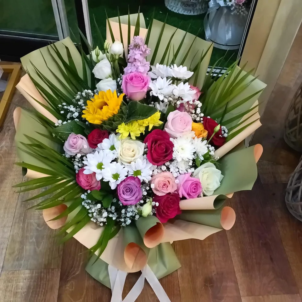 Large mixed bouquet framed by long palm fronds and peach-green wrapping