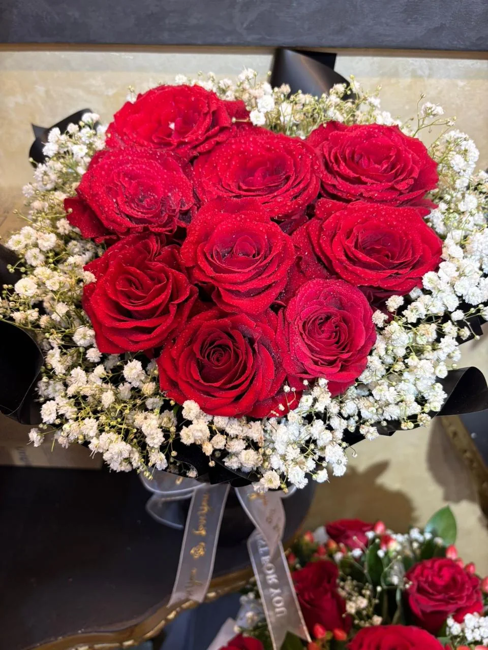 Round red rose bouquet edged with baby's breath and dark wrapping