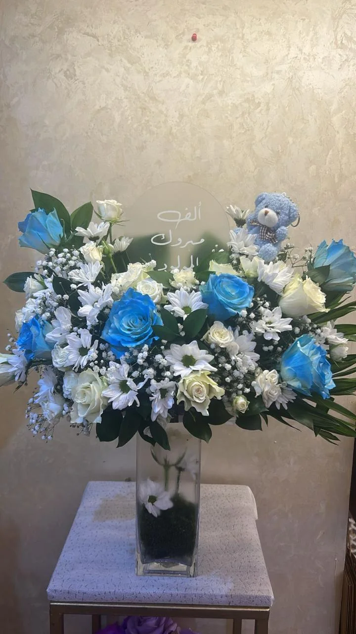 Tall newborn-boy flower stand with blue and white blooms, a teddy and Arabic greeting
