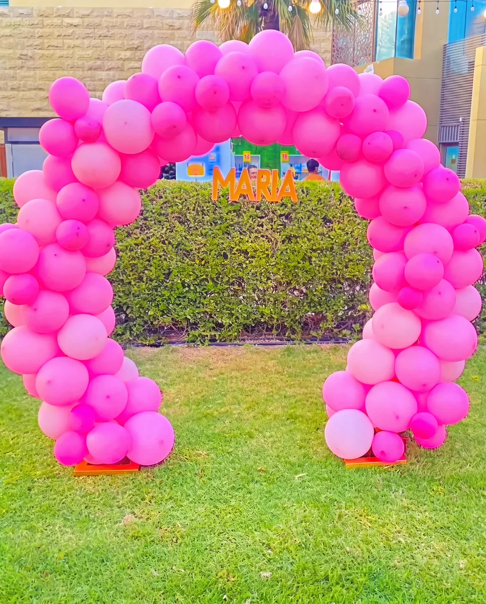 Bright-pink outdoor balloon arch with a personalized name