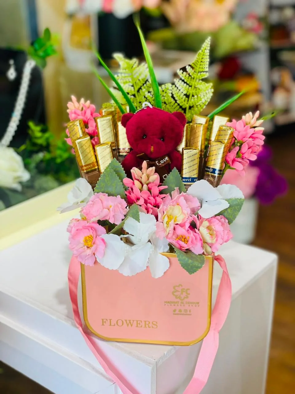 Pink flower gift bag with mixed blooms, wrapped chocolates and a small red teddy