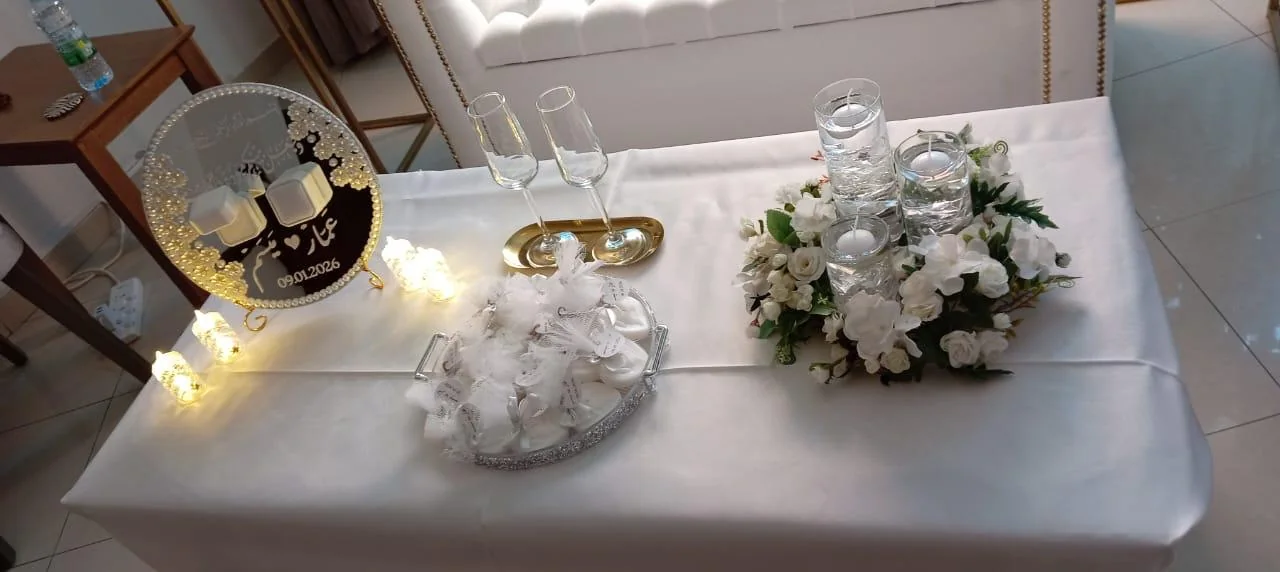 Proposal table with white satin, paired glasses, candles, white flowers and a personalized plaque