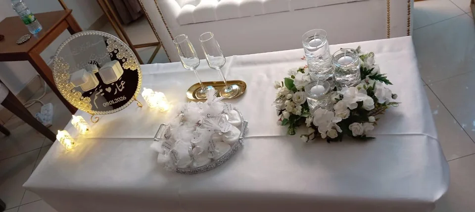 Proposal table with white satin, paired glasses, candles, white flowers and a personalized plaque