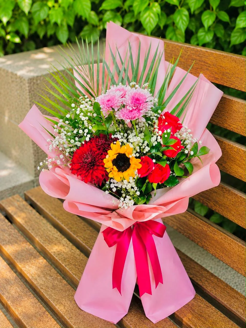 Pink-wrapped bouquet with a sunflower and mixed pink, red and white blooms
