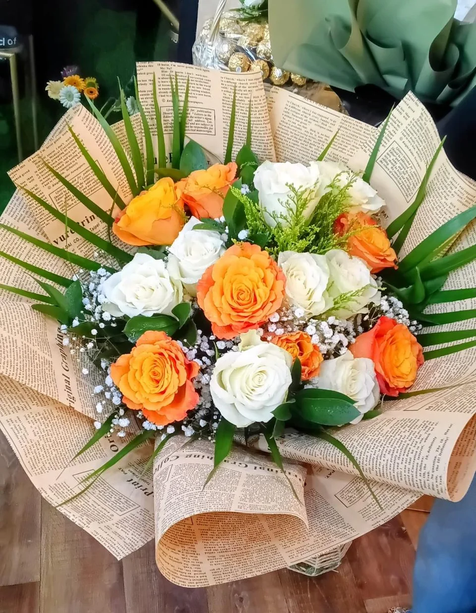 Vintage newspaper-wrapped bouquet with orange and white roses and palm leaves