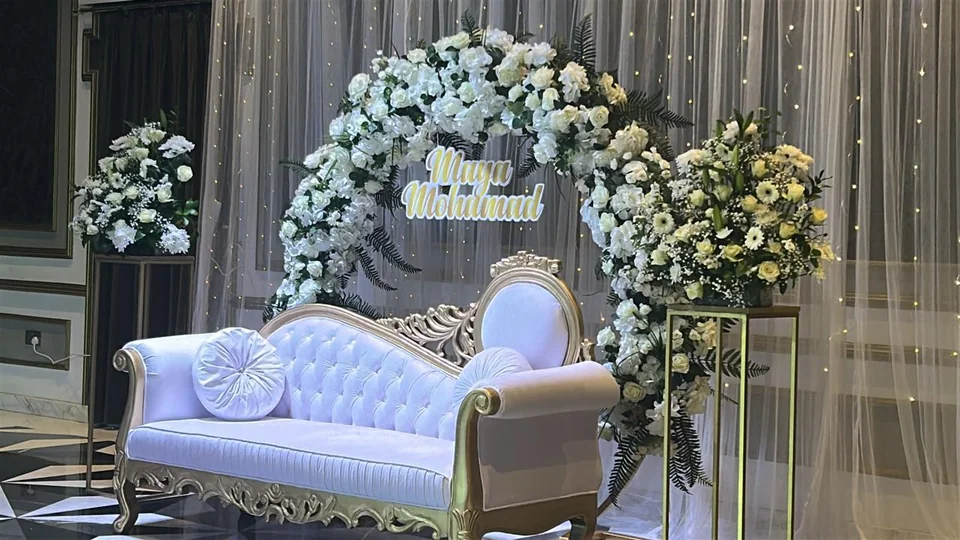 Wedding stage with white bridal sofa, floral arch, side arrangements and couple names