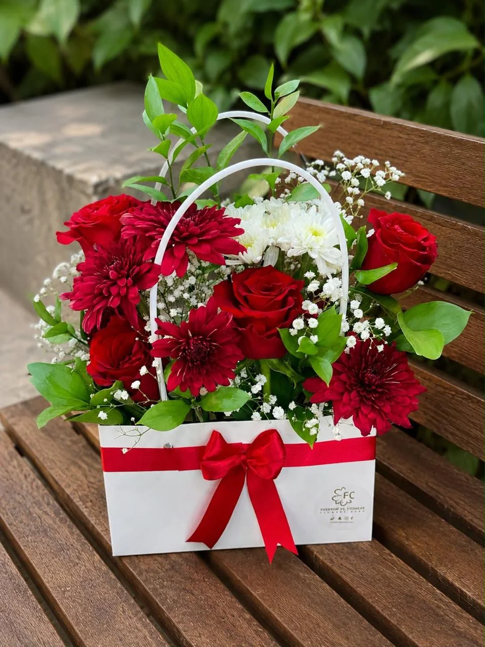 White handled flower bag with red roses, red and white blooms and a red bow